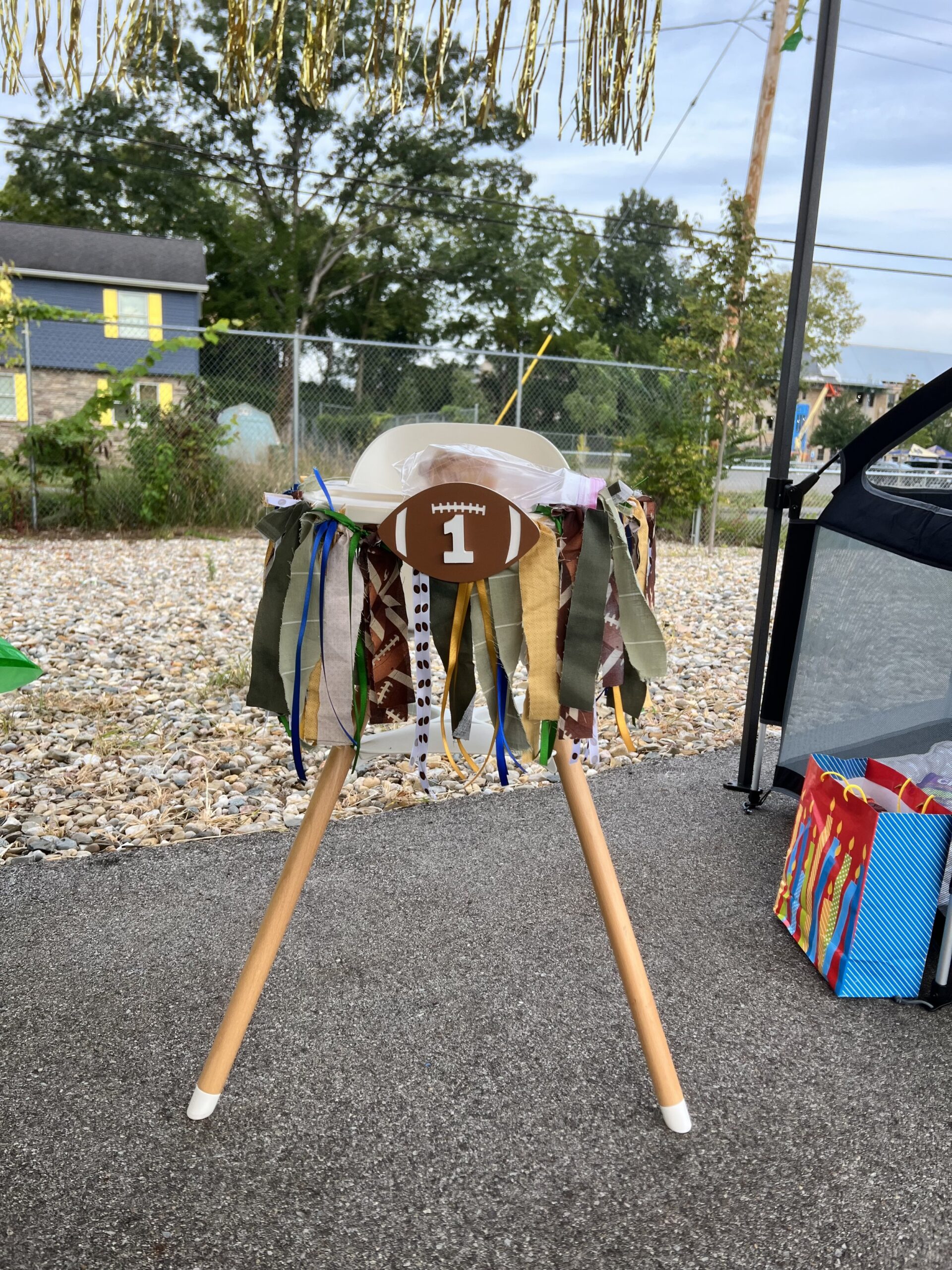 Highchair with a football themed highchair garland with a central football with the number 1 on it and yellow, green, blue, and white ribbon hanging.