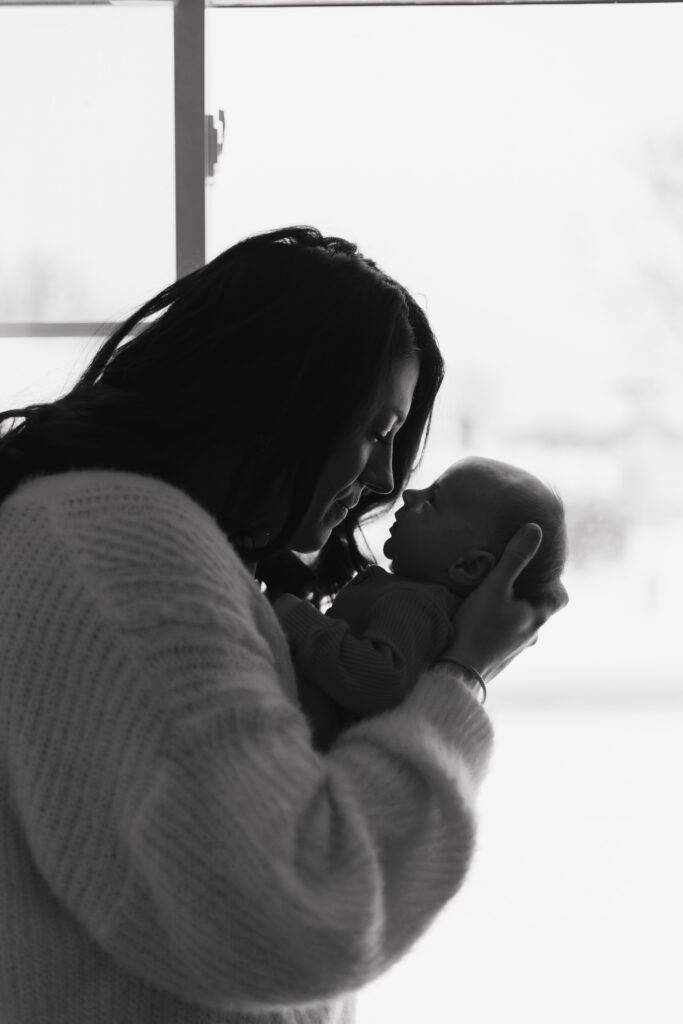 Side profile view of mom holding her newborn baby, noses touching, black and white picture, soft background. 