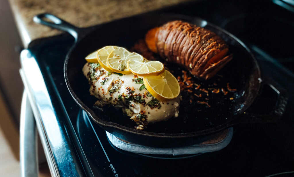 Chicken with lemons and parsley, and a hasselback potato in a cast-iron skillet on a stove.
