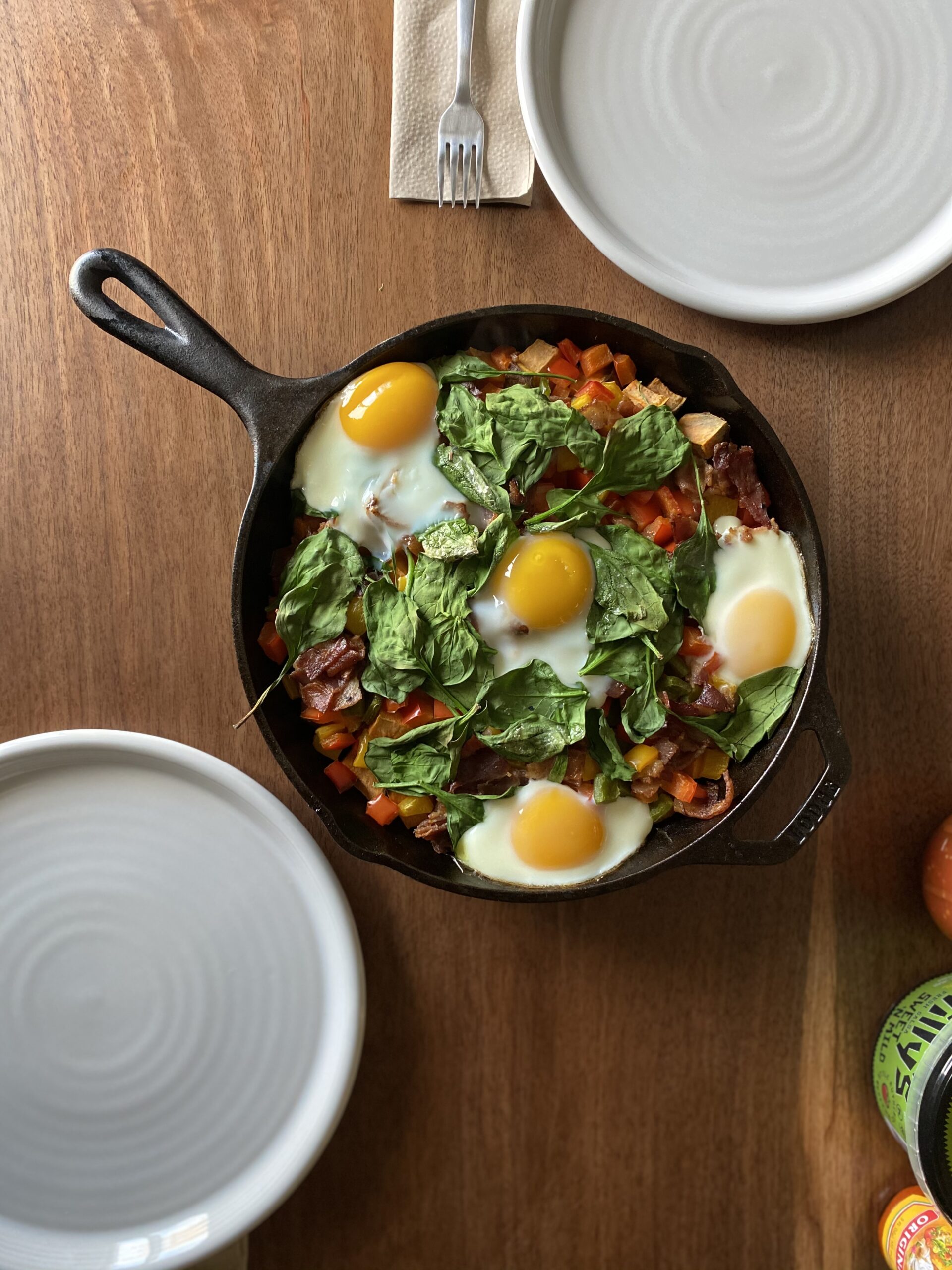 Egg skillet with spinach, tomatoes, peppers in a cast iron skillet on a wooden table.