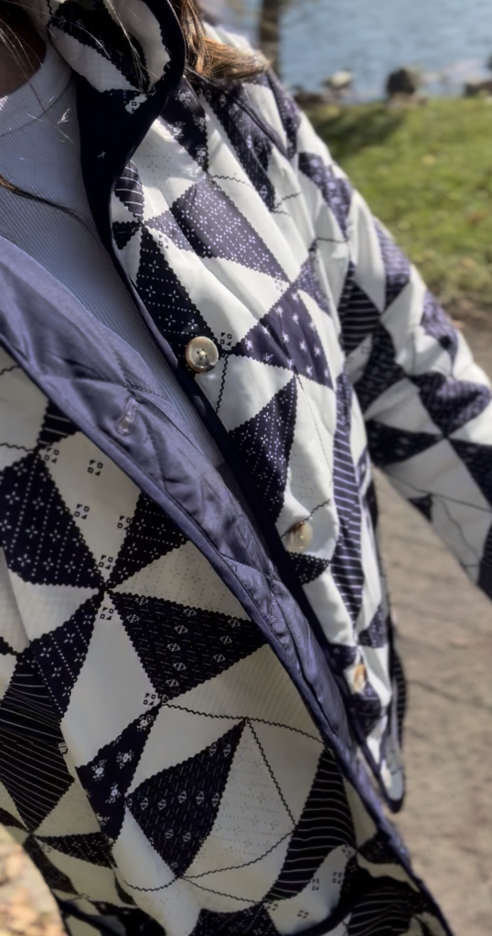 Side profile of navy blue quilted jacket with button detail and quilt detail.