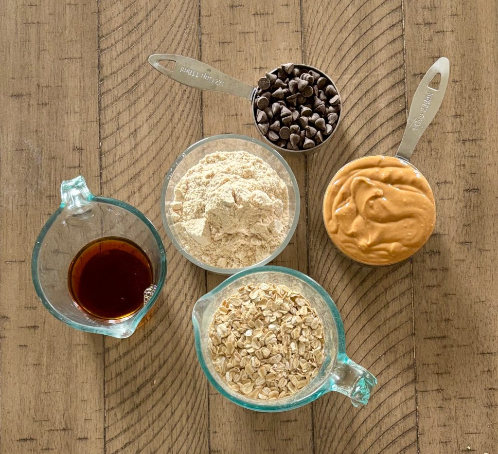 Top down view of ingredients, honey, oats, peanut butter, protein powder, and chocolate chips. 