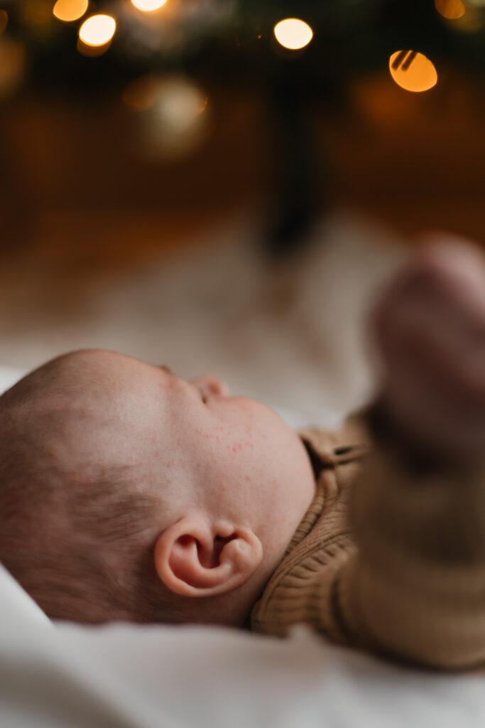 Baby looking off at a Christmas tree that is lit and sparkling. 