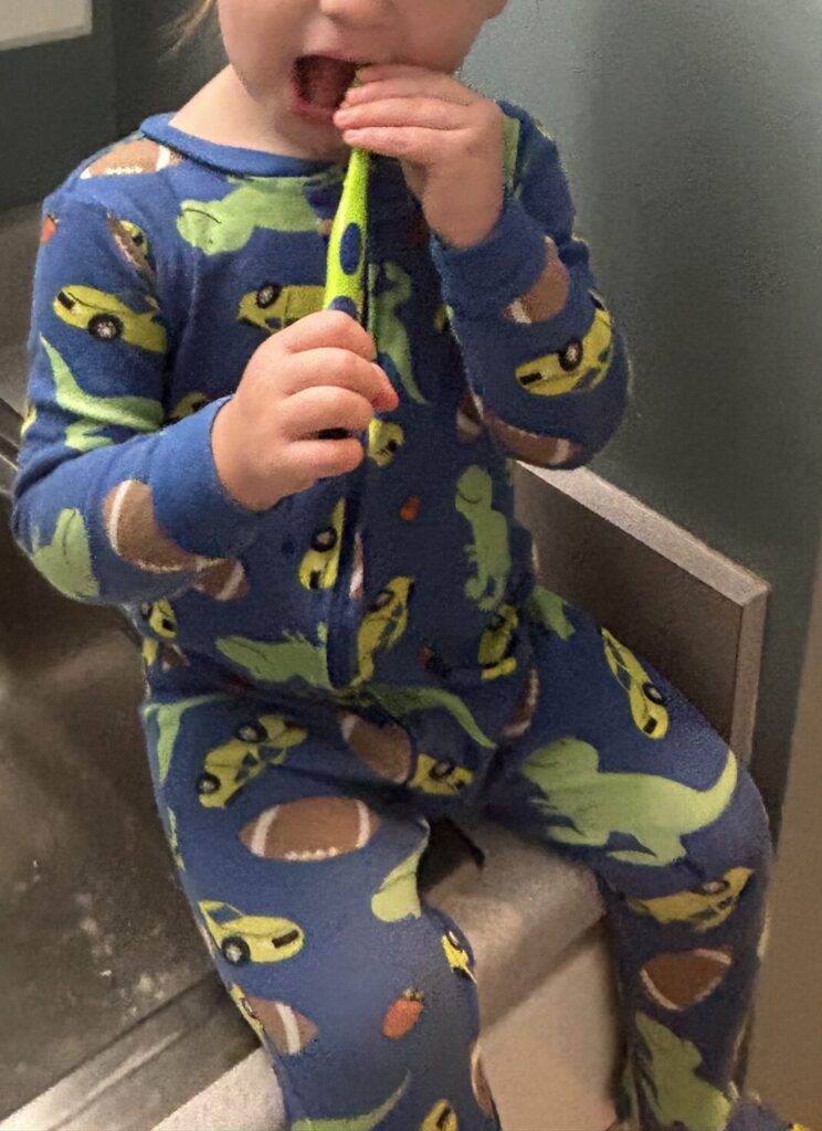 A child getting ready for bedtime by brushing their teeth at the bathroom sink in their pajamas.