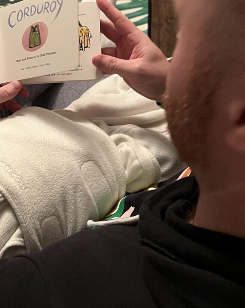 A behind view of a parent reading to a baby swaddled before bedtime as part of a bedtime routine.