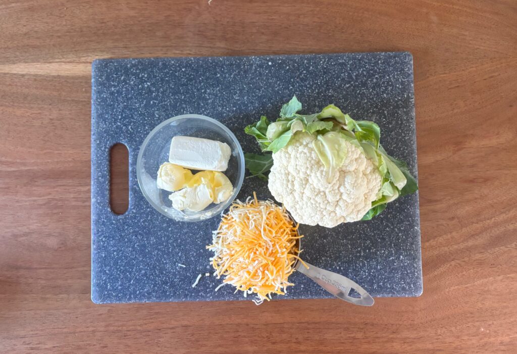 Top down veiw of Cauliflower mash ingredients of shredded cheese, cauliflower, cream cheese and butter.