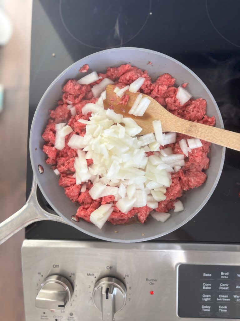 Top-down view of diced onions in ground beef being browned in a skillet.