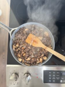 Top-down view of browned beef for shepherds pie with onions, optional mushrooms, and homemade Worcestershire sauce.