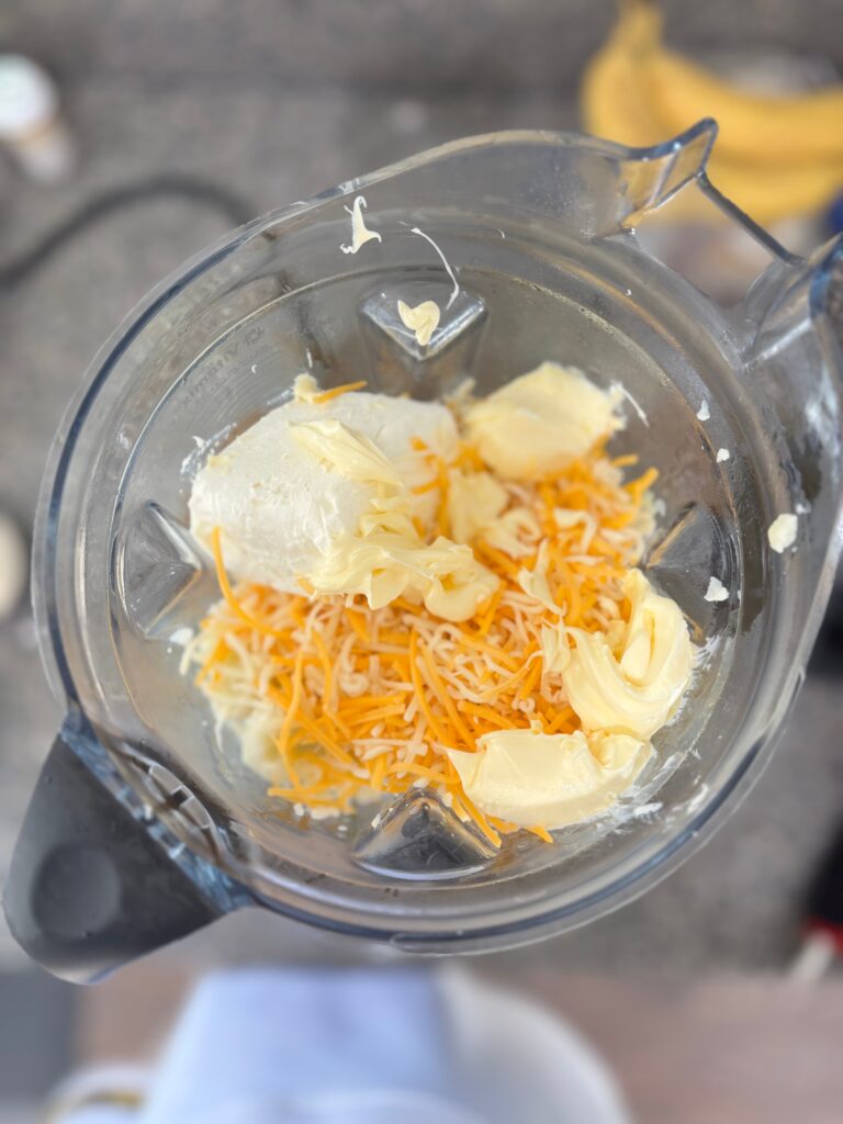 Top-down view of Cauliflower mash ingredients of butter, cream cheese and cheese in a blender ready to be blended.