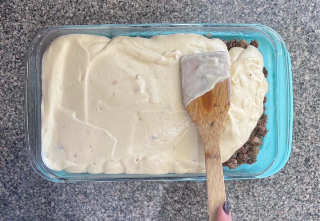 Top-down view of cauliflower mash being spread on top of meat mixture for Shepherds pie.