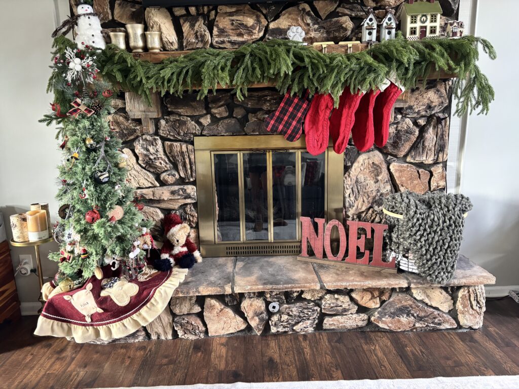 Front facing view of a fireplace with a wood mantel and a tree with pine garland on the mantel.