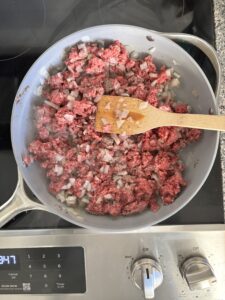Top-down view of ground beef, onion, garlic, salt and pepper, being browned for chili that is low carb and high in protein.