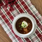 Top-down view of low-carb chili in a bowl with sour cream, shredded cheddar cheese, and green onions.