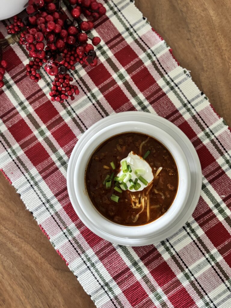 Top-down view of low-carb chili in a bowl with sour cream, shredded cheddar cheese, and green onions.