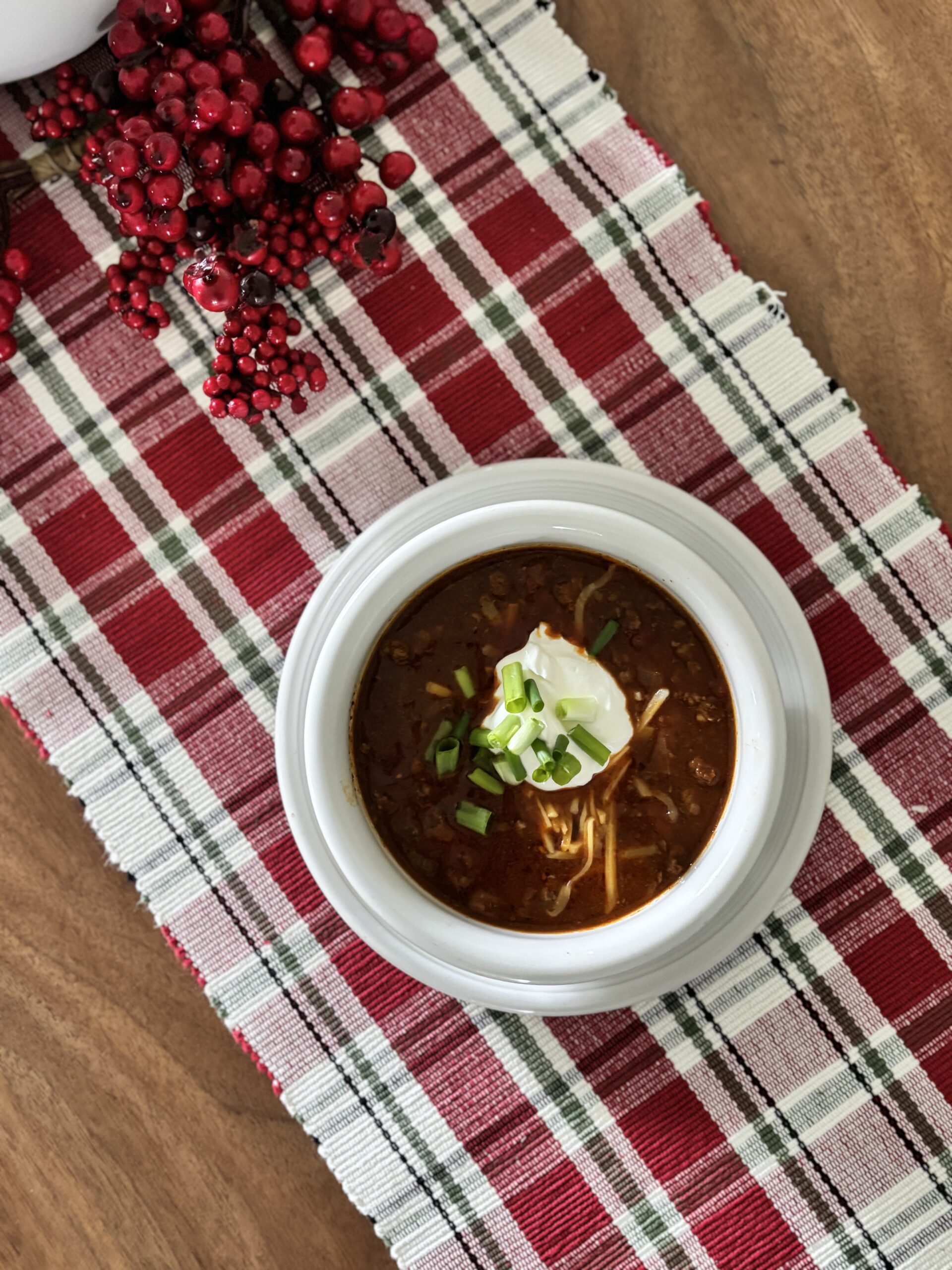 Top-down view of low-carb chili in a bowl with sour cream, shredded cheddar cheese, and green onions.