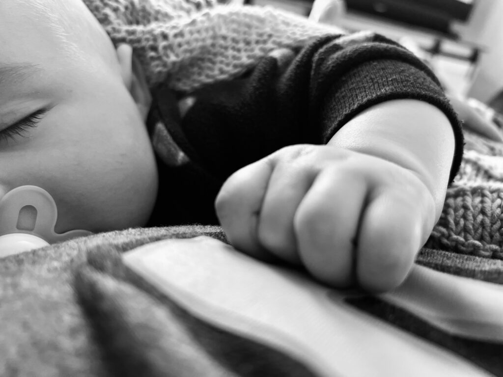 A close up few of a baby sleeping at bedtime with a pacifier in and a small little baby hand.